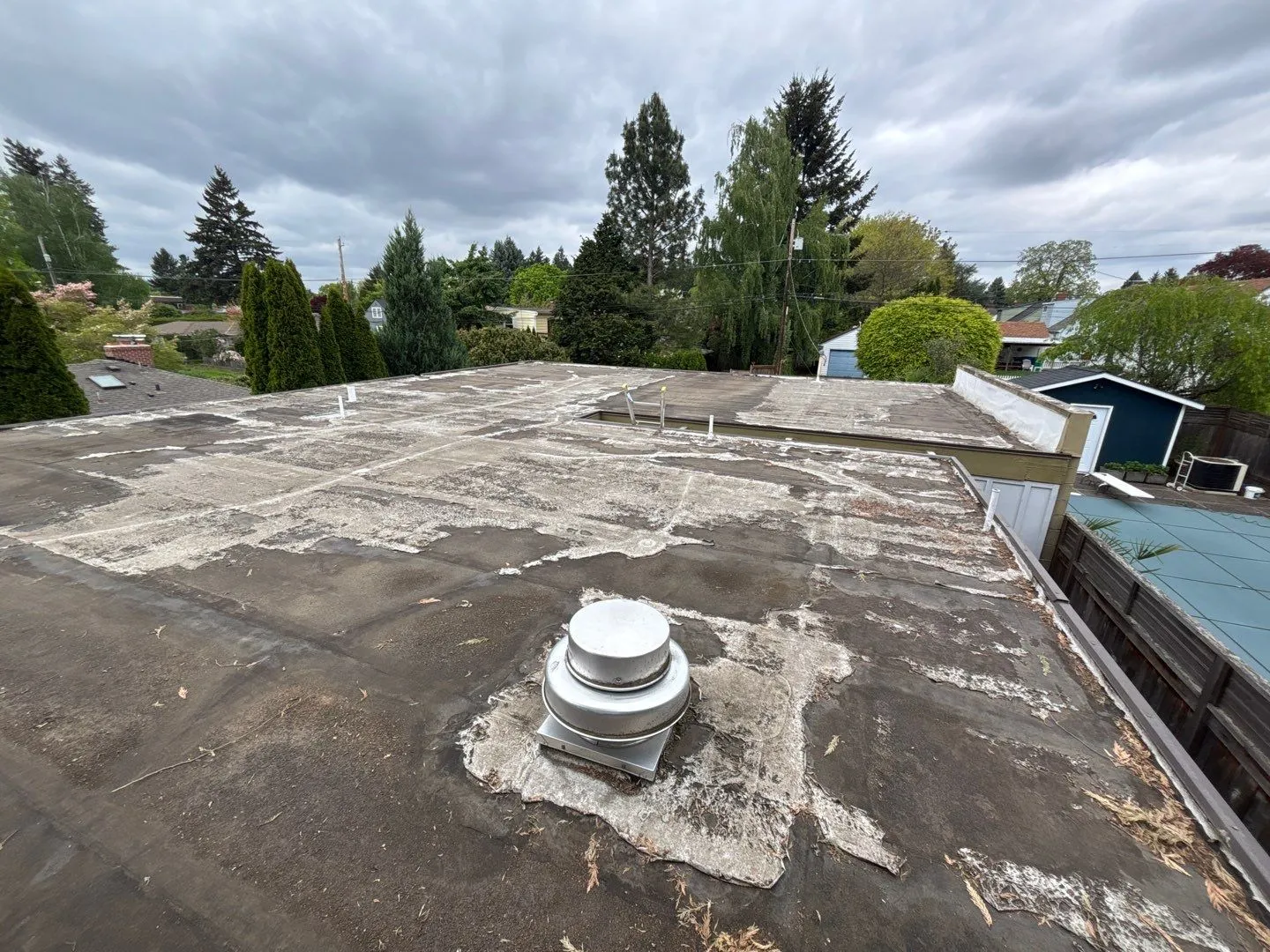 An old flat-roof membrane across a whole roof, weathered grey with chalky white patches from years of sun