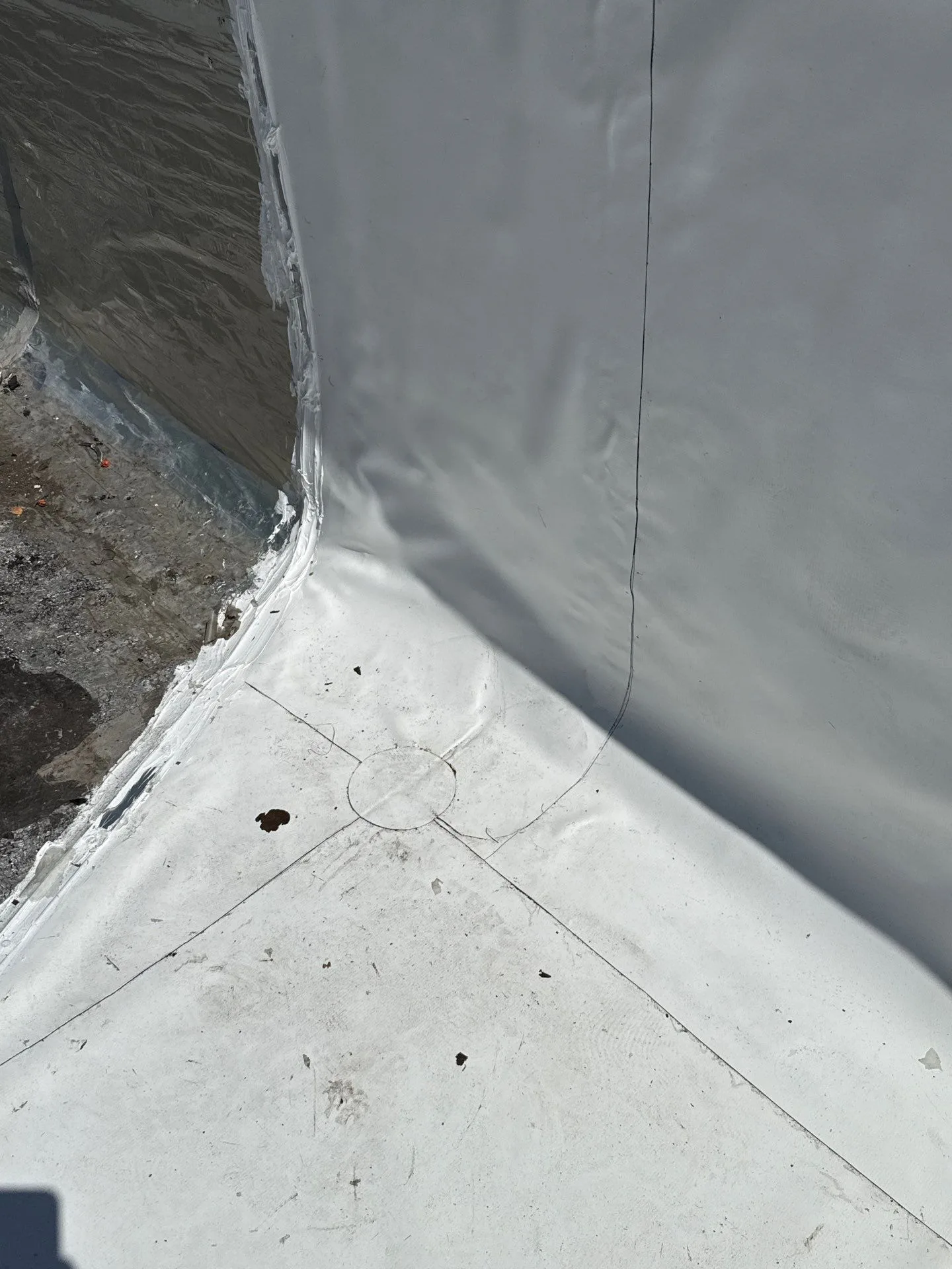 A white flat-roof membrane carried up the parapet wall and welded around a tight inside corner, the field and wall sheets sealed together in one continuous waterproof line.