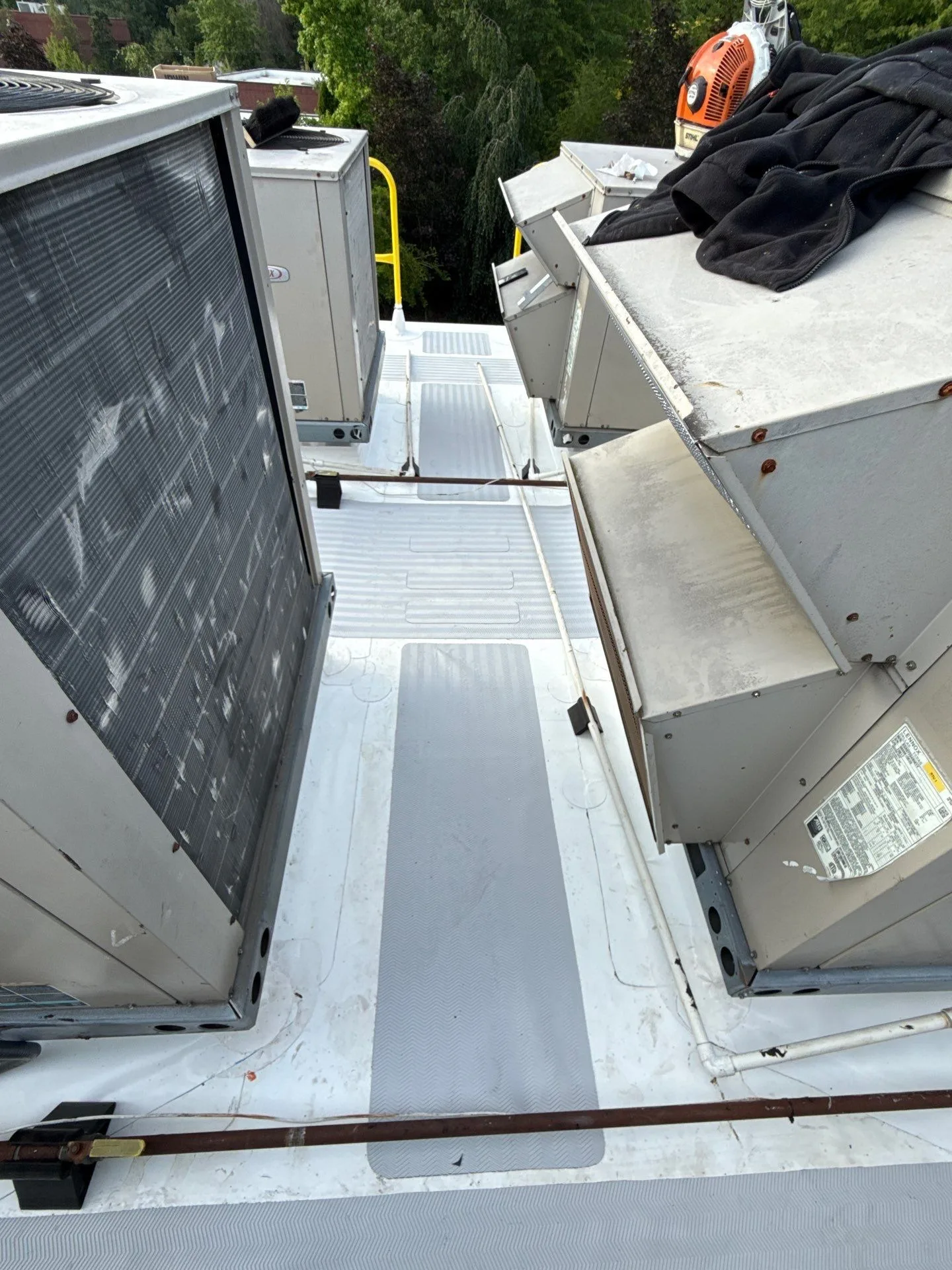Looking down a fresh white flat-roof membrane between two rows of rooftop HVAC units, with gray walk pads laid down the center and gas lines running across the surface.