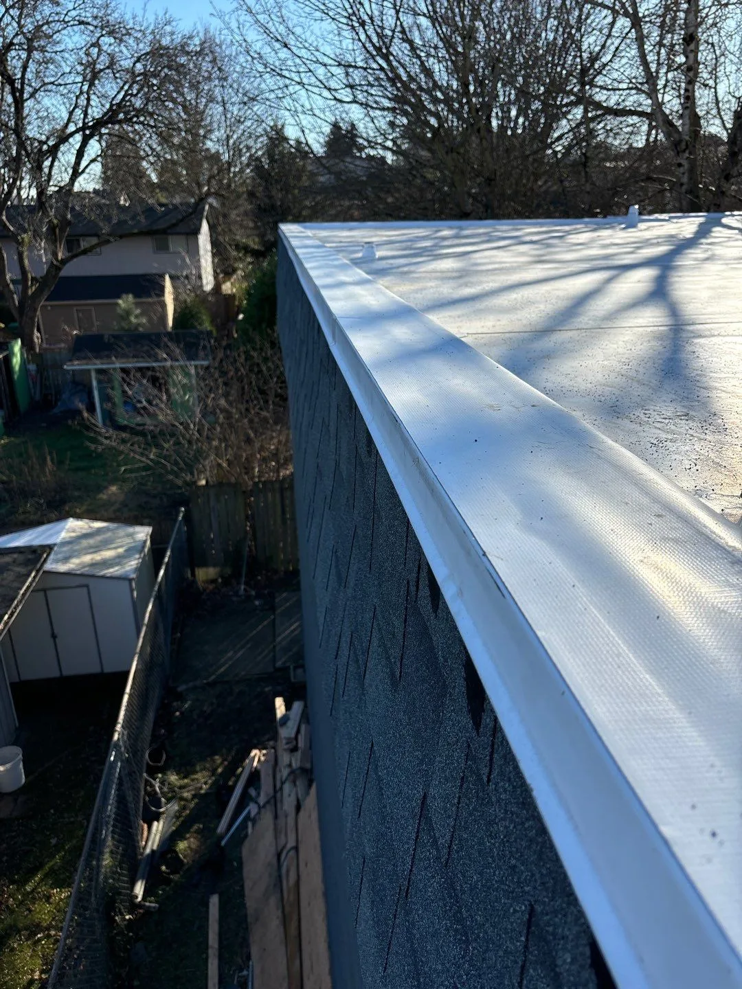 A finished white flat roof membrane carried cleanly to the roof edge above a residential building.