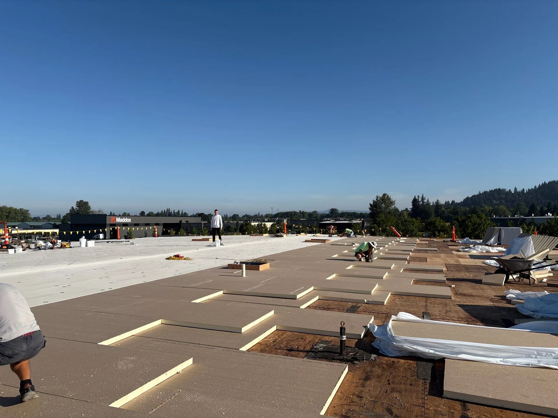 A full reroof in progress, with crew members installing insulation and white membrane across a large flat roof.