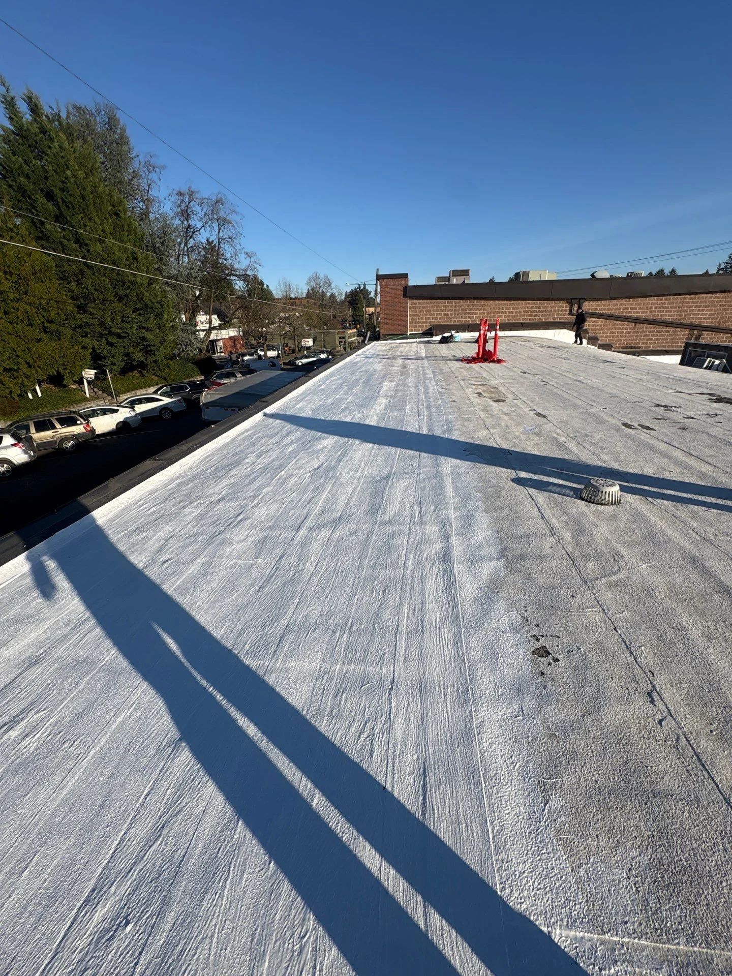 A modified-bitumen commercial flat roof freshly coated in white silicone, the seamless skin running the full length of the roof past a drain and vent under a clear blue sky.