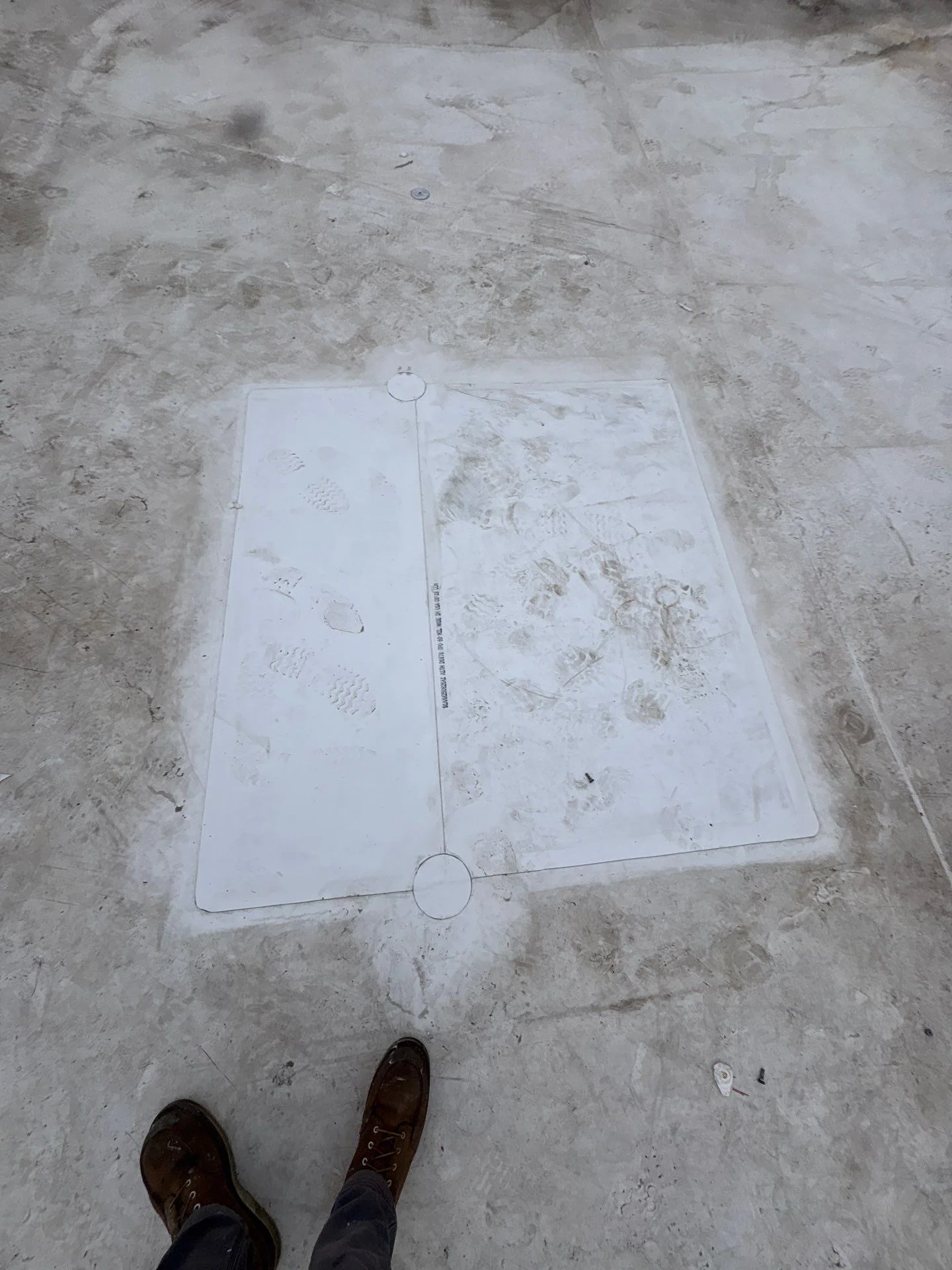 A fresh bright white sheet of membrane laid down on top of an old weathered flat roof, welded in place with round spots at top and bottom and stamped with crisp boot prints from the crew.