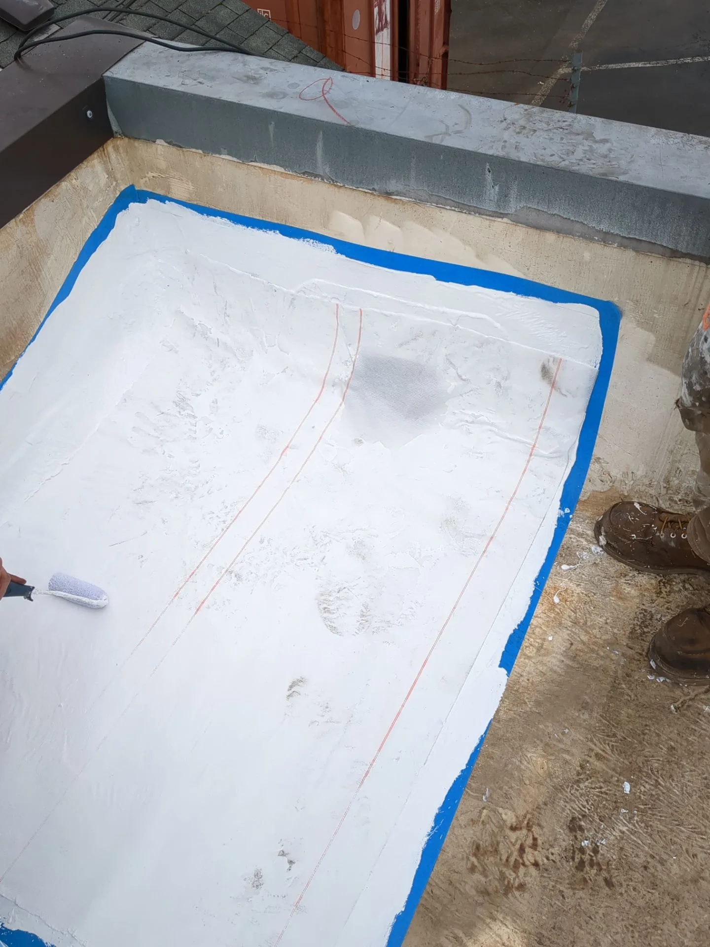 A roofer rolling fresh white silicone onto a taped-off area of a flat roof.