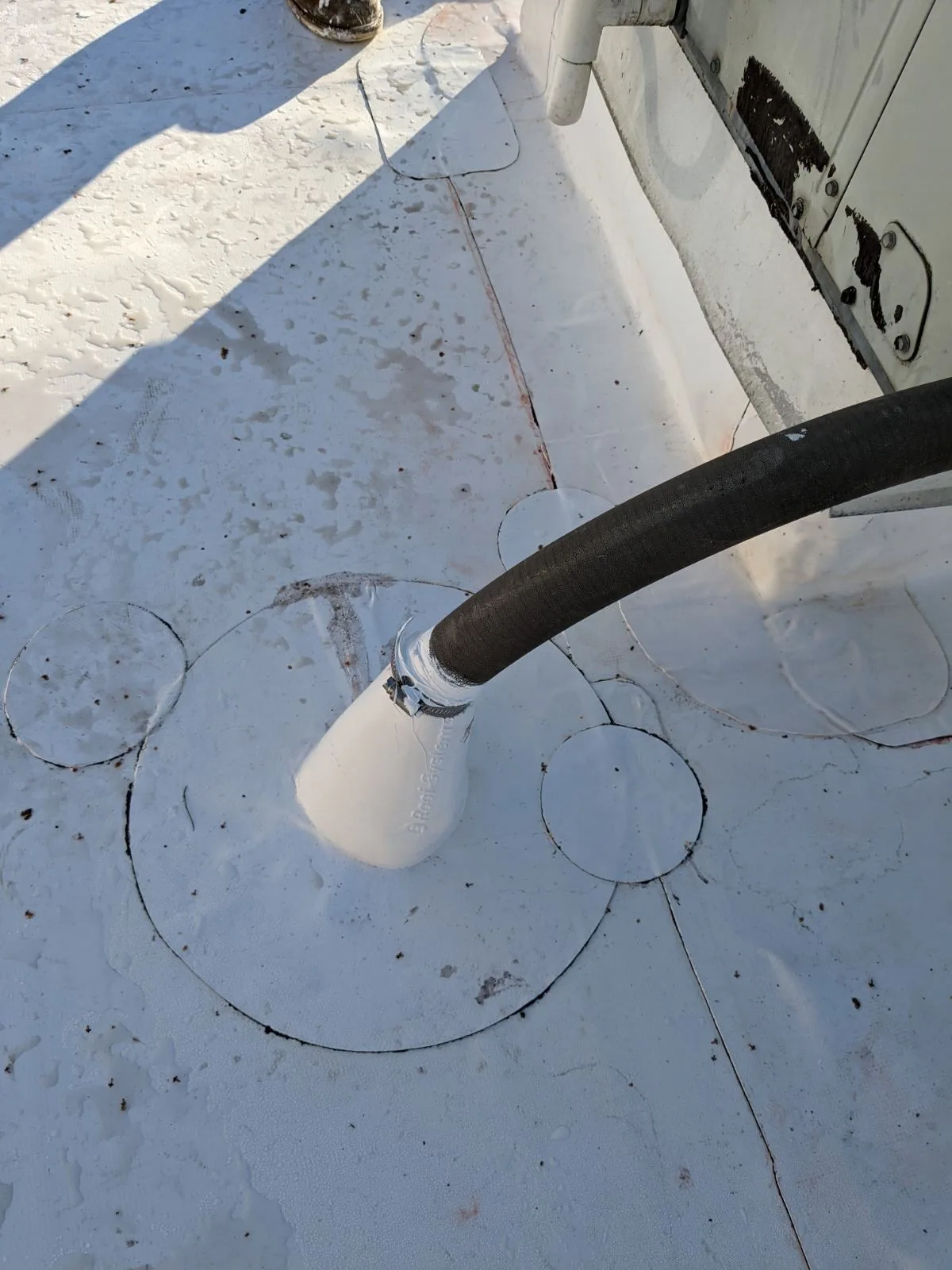 A pipe coming through a flat roof, sealed white around its collar.