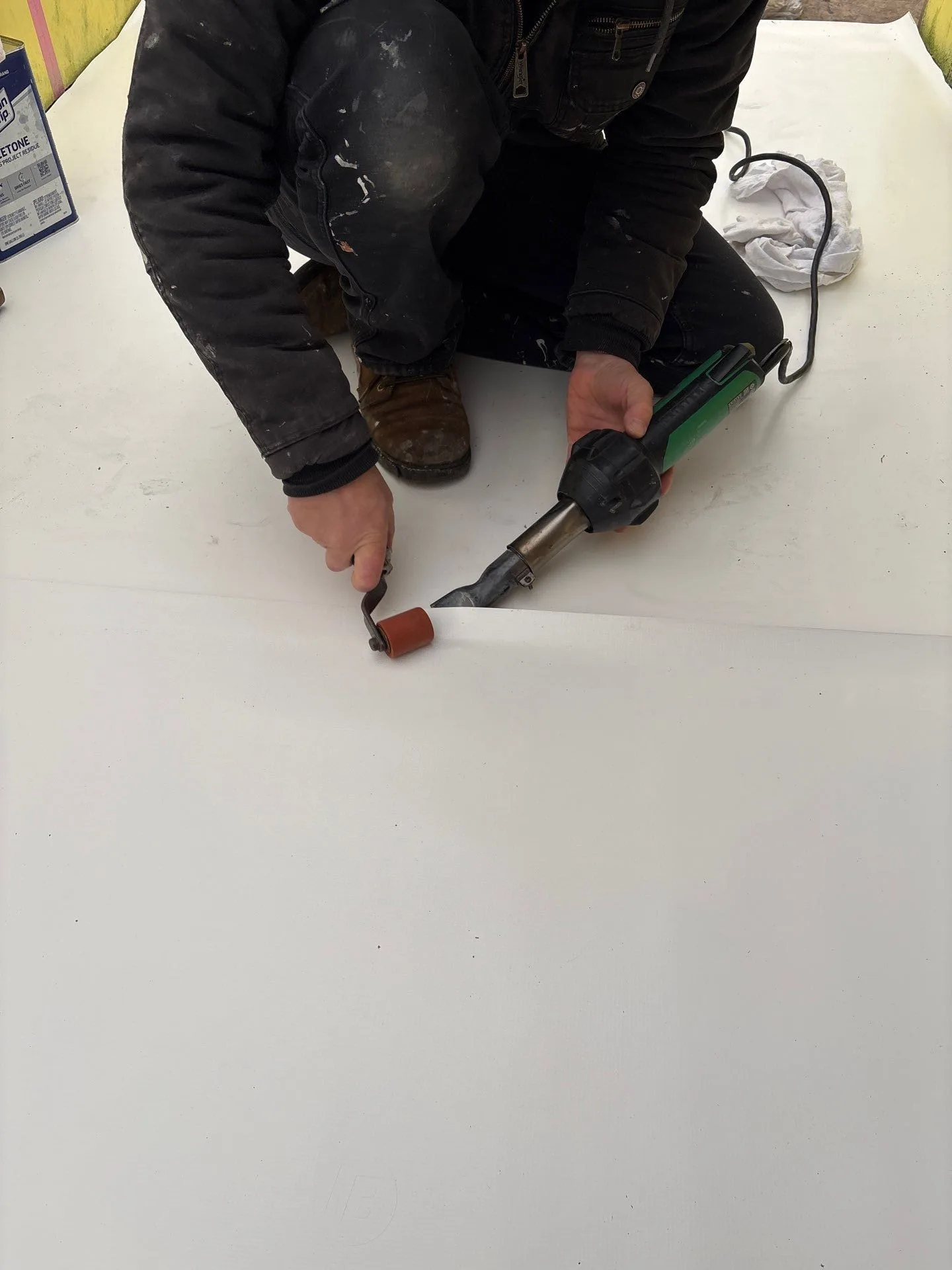 A roofer running a heat welder and roller along a seam in white membrane.