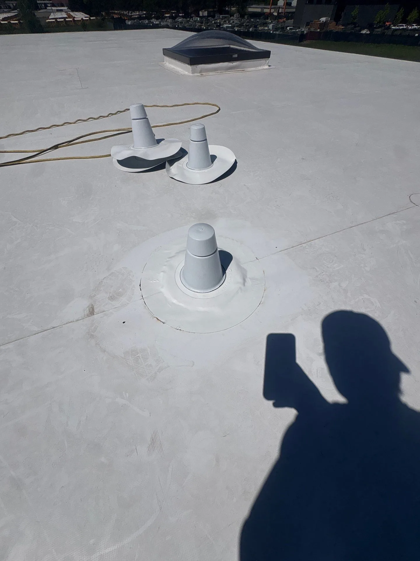 Freshly sealed pipe penetrations on a sound white flat roof, kept in service.
