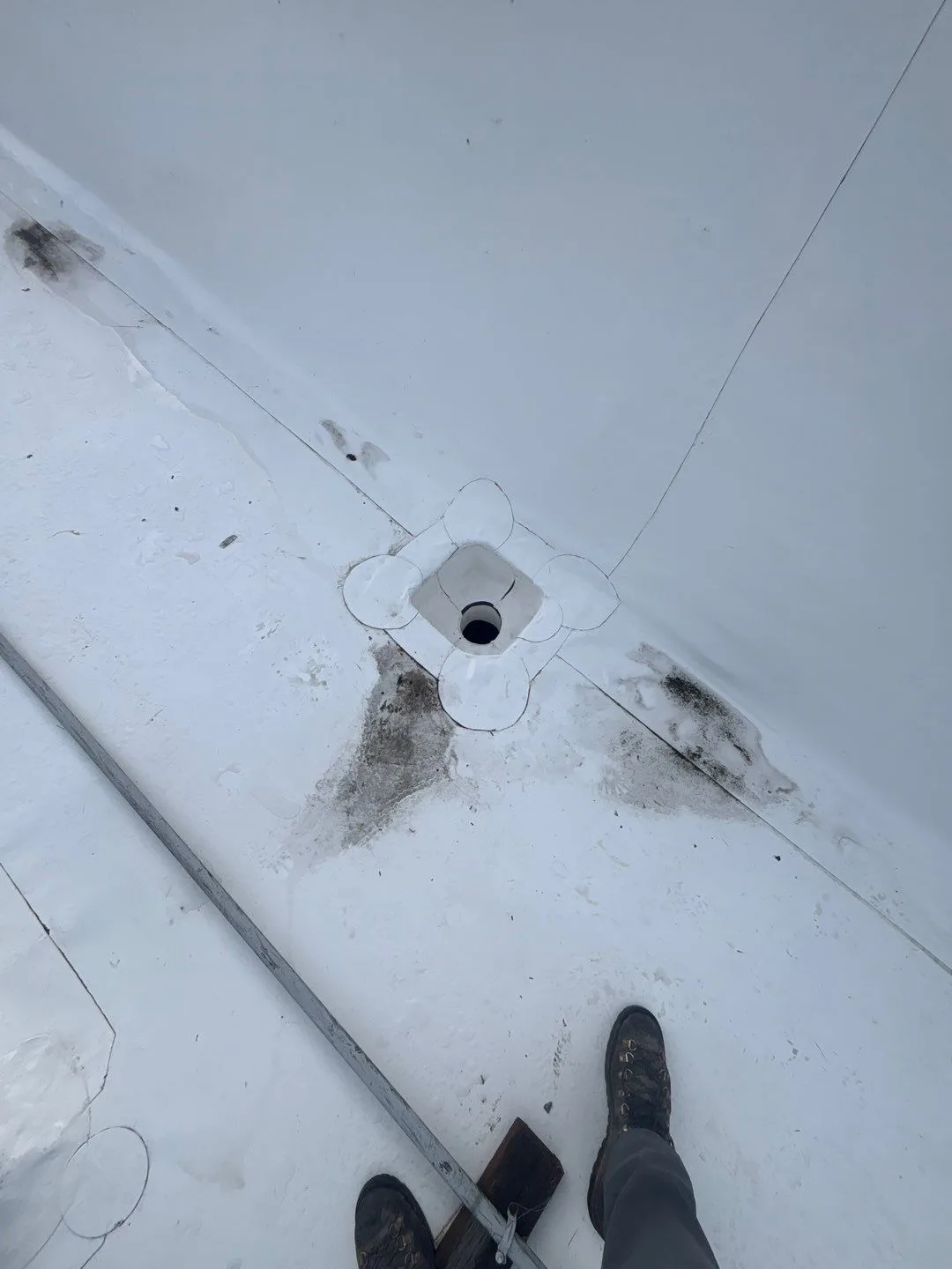 A drain opening welded into a white flat-roof membrane at a wall corner, with the surrounding flashing sealed flush.
