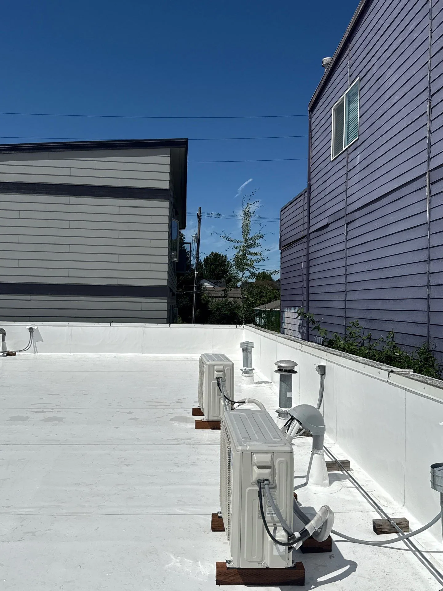 A white flat roof with mini-split condensers, vent pipes, and a gas line, each penetration sealed where it passes through the membrane.