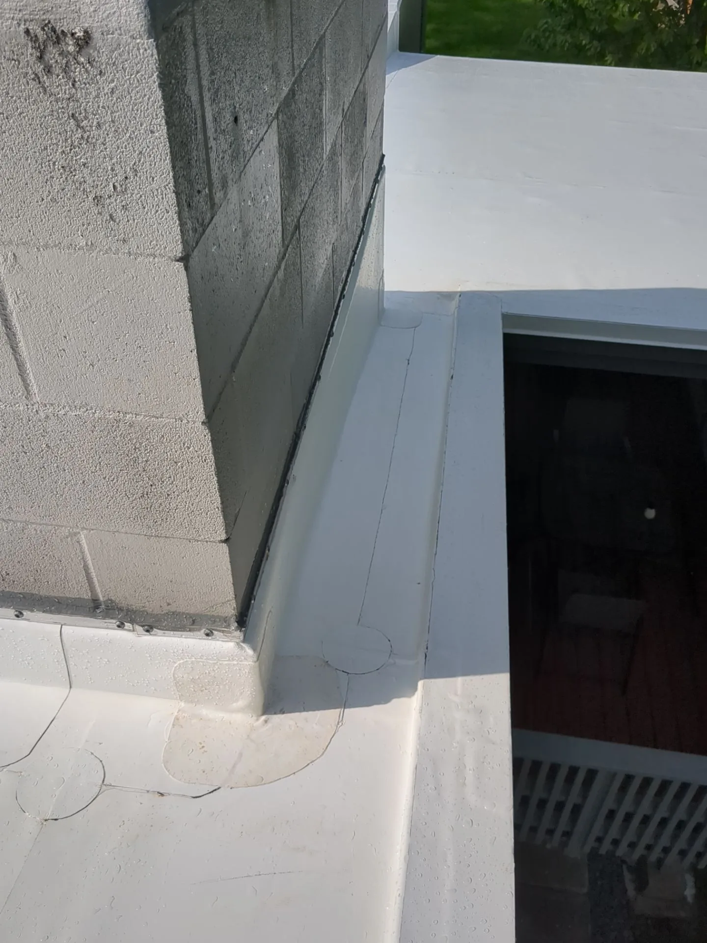 A white roof membrane carried up the parapet walls and around an inside corner, locked down by a fastened termination bar at the base, beside a roof hatch opening.
