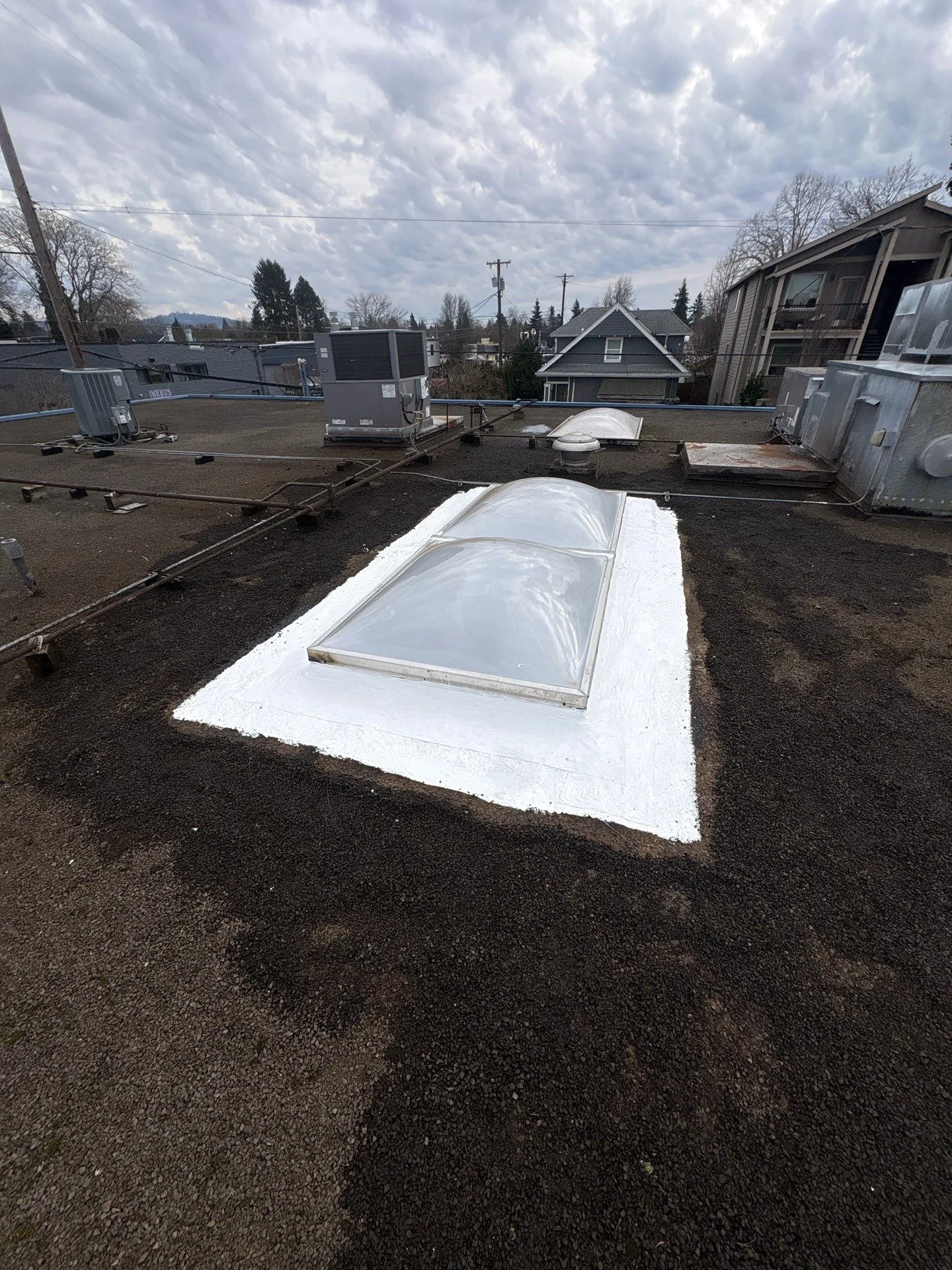 A skylight on a flat roof with fresh white silicone coating sealing its base into the surrounding membrane.